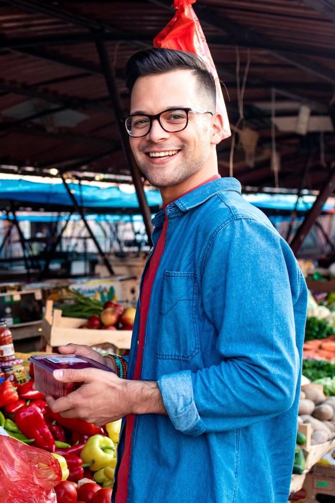 Portrait of young man standing in front of a vegetable counter in an outdoor market.