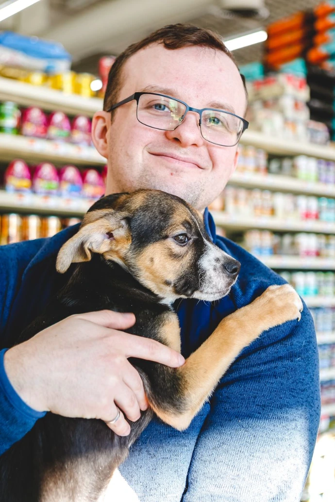 Man Holds Small Dog in Store Aisle